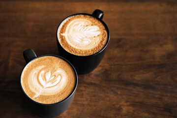 Two cappuccino coffee with latte art on wooden table. Black cups and beautiful milk foam. Soft focus