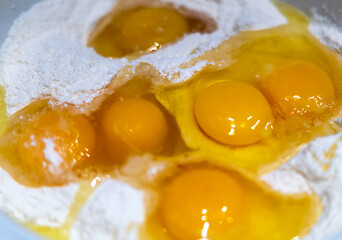 Fresh raw, yellow chicken eggs in flour close-up. Mix the broken raw eggs and wheat flour with a whisk to make the dough. The concept of healthy eating. Food background. I bake bread. Organic product.