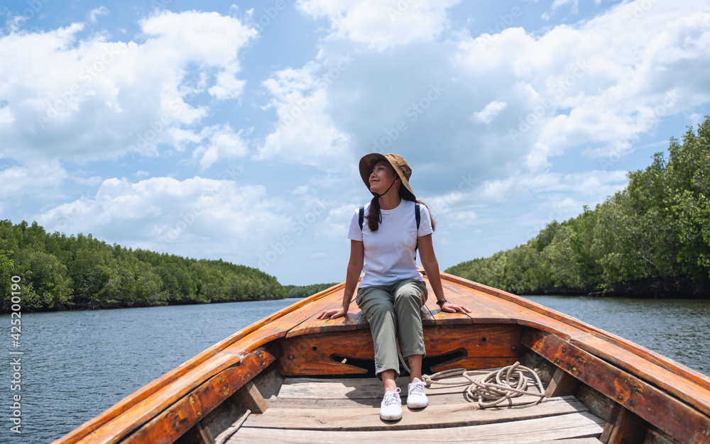 Portrait image of a beautiful young asian woman sitting on a long tail boat while traveling the sea and mangrove forest - obrazy, fototapety, plakaty 