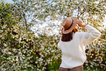 Smiling woman with the hat posing in blooming spring park. The concept of relax, travel, freedom and spring vacation. Fashion style.