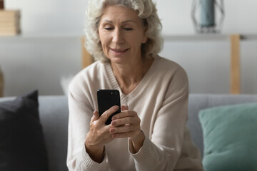 happy older woman using smartphone for video call from home, reading message on mobile phone and rec