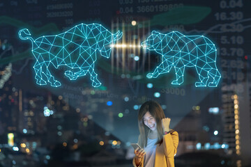 Asian businesswoman using smart mobile phone with smile action showing Bull and Bear polygonal shape writing by lines and dots over Stock market exchange and Trading graph on the cityscape background