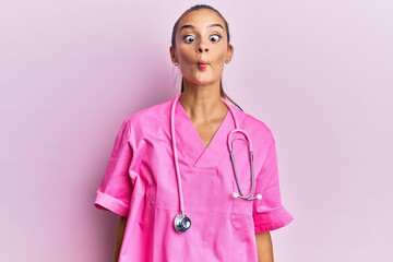 Wall Mural - Young hispanic woman wearing doctor uniform and stethoscope making fish face with lips, crazy and comical gesture. funny expression.