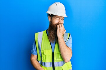 Canvas Print - Redhead man with long beard wearing safety helmet and reflective jacket looking stressed and nervous with hands on mouth biting nails. anxiety problem.