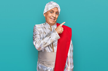 Poster - Senior hispanic man wearing tradition sherwani saree clothes cheerful with a smile of face pointing with hand and finger up to the side with happy and natural expression on face