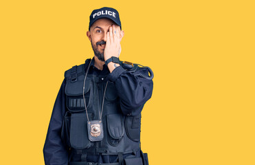 Poster - Young handsome man wearing police uniform covering one eye with hand, confident smile on face and surprise emotion.