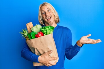 Sticker - Caucasian young man with long hair holding paper bag with groceries celebrating achievement with happy smile and winner expression with raised hand