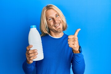 Sticker - Caucasian young man with long hair holding liter bottle of milk smiling happy and positive, thumb up doing excellent and approval sign