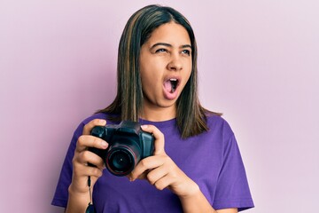 Poster - Young latin woman using reflex camera angry and mad screaming frustrated and furious, shouting with anger. rage and aggressive concept.