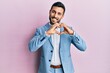 © Krakenimages.com - Young hispanic businessman wearing business jacket smiling in love doing heart symbol shape with hands. romantic concept.