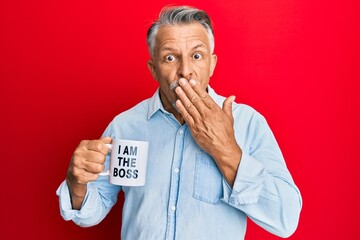 Canvas Print - Middle age grey-haired man drinking from i am the boss coffee cup covering mouth with hand, shocked and afraid for mistake. surprised expression