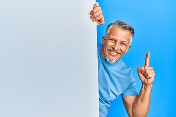 Sticker - Middle age grey-haired man holding blank empty banner smiling with an idea or question pointing finger with happy face, number one