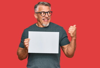 Poster - Middle age grey-haired man holding blank empty banner pointing thumb up to the side smiling happy with open mouth