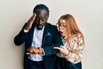 Canvas Print - Young interracial couple wearing business and elegant clothes looking at the watch time worried, afraid of getting late