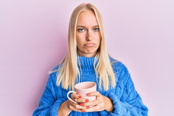 Canvas Print - Young blonde girl wearing winter sweater and drinking a cup of hot coffee depressed and worry for distress, crying angry and afraid. sad expression.