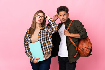 Young student couple isolated on white background having doubts while scratching head