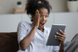 © fizkes - Stunned young African American woman shocked by unexpected news or message online on tablet. Amazed millennial biracial female look at screen surprised by unbelievable text or email on pad device.