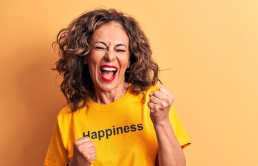 Middle age beautiful woman wearing t-shirt with happiness word over yellow background celebrating surprised and amazed for success with arms raised and eyes closed