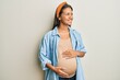© Krakenimages.com - Beautiful hispanic woman expecting a baby, touching pregnant belly looking away to side with smile on face, natural expression. laughing confident.