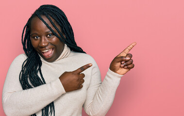 Sticker - Young black woman with braids wearing casual winter sweater smiling and looking at the camera pointing with two hands and fingers to the side.