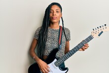 African American Woman Playing Electric Guitar Relaxed With Serious Expression On Face. Simple And Natural Looking At The Camera.