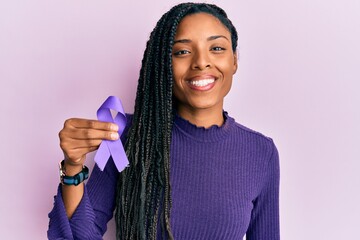 African american woman holding purple ribbon awareness looking positive and happy standing and smiling with a confident smile showing teeth