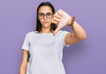 Young hispanic woman wearing casual white t shirt looking unhappy and angry showing rejection and negative with thumbs down gesture. bad expression.