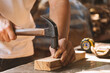 Close-up of carpenter using hammer nailing nail to wood plank at factory of wood.