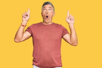 Poster - Handsome middle age man wearing casual clothes amazed and surprised looking up and pointing with fingers and raised arms.