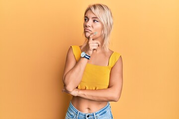 Poster - Young blonde girl wearing casual clothes with hand on chin thinking about question, pensive expression. smiling with thoughtful face. doubt concept.