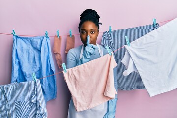 Poster - African american woman with braided hair washing clothes at clothesline asking to be quiet with finger on lips. silence and secret concept.