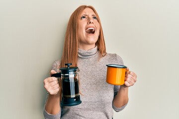 Wall Mural - Young irish woman drinking italian coffee angry and mad screaming frustrated and furious, shouting with anger looking up.