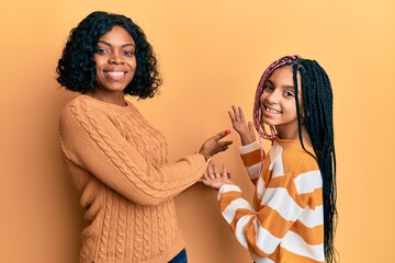 Sticker - Beautiful african american mother and daughter wearing wool winter sweater inviting to enter smiling natural with open hand