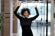 © fizkes - Overjoyed young African American female employee or worker dance in office hallway enjoy Friday fun. Happy smiling millennial biracial businesswoman celebrate job success or work achievement.