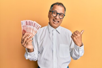 Canvas Print - Middle age indian man holding 100 new taiwan dollars banknotes pointing thumb up to the side smiling happy with open mouth