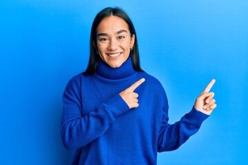 Wall Mural - Young asian woman wearing casual winter sweater smiling and looking at the camera pointing with two hands and fingers to the side.