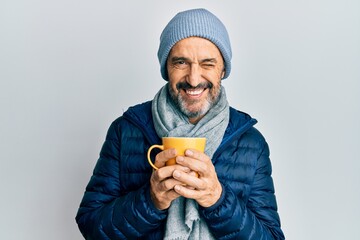 Poster - Middle age hispanic man wearing winter scarf and drinking a cup of hot coffee winking looking at the camera with sexy expression, cheerful and happy face.