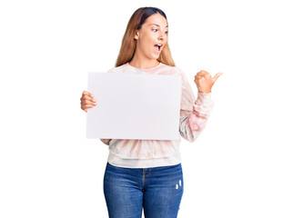 Sticker - Beautiful young woman holding blank empty banner pointing thumb up to the side smiling happy with open mouth