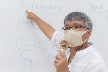 Speaker Professor female Asian teaching explain wear Medical face mask for safety speaking microphone at whiteboard in classroom in university. Teacher in Health care prevent COVID-19 disease epidemic