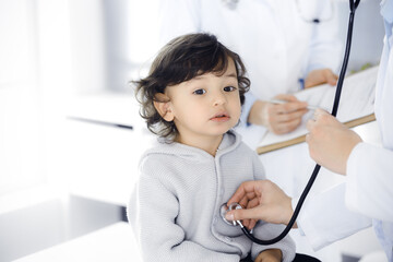 Woman-doctor examining a child patient by stethoscope. Cute arab toddler at physician appointment. Medicine concept