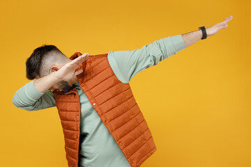 Wall Mural - Young caucasian fun man 20s wearing orange vest mint sweatshirt glasses doing dab hip hop dance hands move gesture youth sign hiding covering face isolated on yellow color background studio portrait