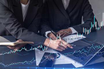 Two traders researching historic data to predict stock market behavior. Women in trading business concept. Forex and financial hologram chart over the table with the document.