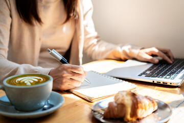 Wall Mural - Young woman with cup of coffee sitting and working on laptop at coffee shop