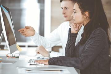 Wall Mural - Business woman and man discussing questions while using computer at workplace in modern office. Teamwork, meeting and brainstorming concept