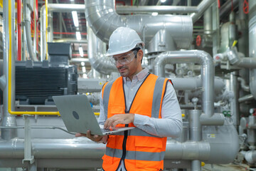 Wall Mural - An engineer man or worker, people using a laptop computer, working in industry factory. Chiller tower or cooling tower in building. System work machine. Condenser Water Supply pipe lines. Ventilation.