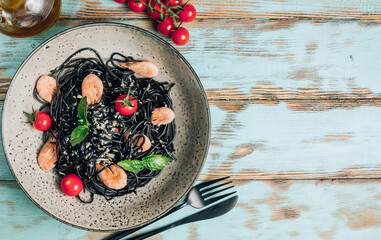 Wall Mural - Black pasta with seafood. Traditional Italian cuisine - pasta with shrimp, tomato and basil in a ceramic plate on a rustic background. Flat lay, top view.