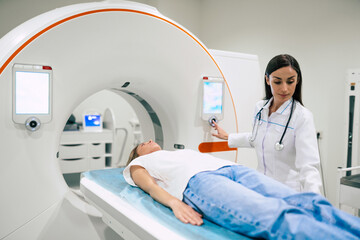 Wall Mural - Professional Doctor Radiologist In Medical Laboratory Controls magnetic resonance imaging or computed tomography or PET Scan with Female Patient Undergoing Procedure.