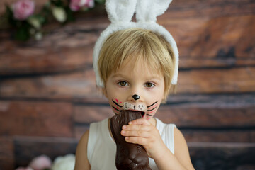 Little toddler boy, child with rabbit painted on the face, eating chocolate bunny