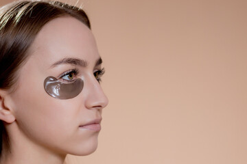 Wall Mural - Portrait of young woman posing with applied black beauty patches under eyes over beige background