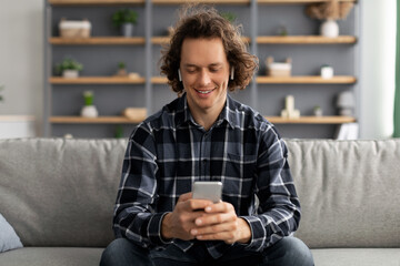 Poster - Positive Guy In Earbuds Using Smartphone Sitting On Sofa Indoor